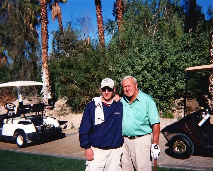 A scanned print of a younger JJ Resnick standing with Arnold Palmer beside golf carts on a desert course.