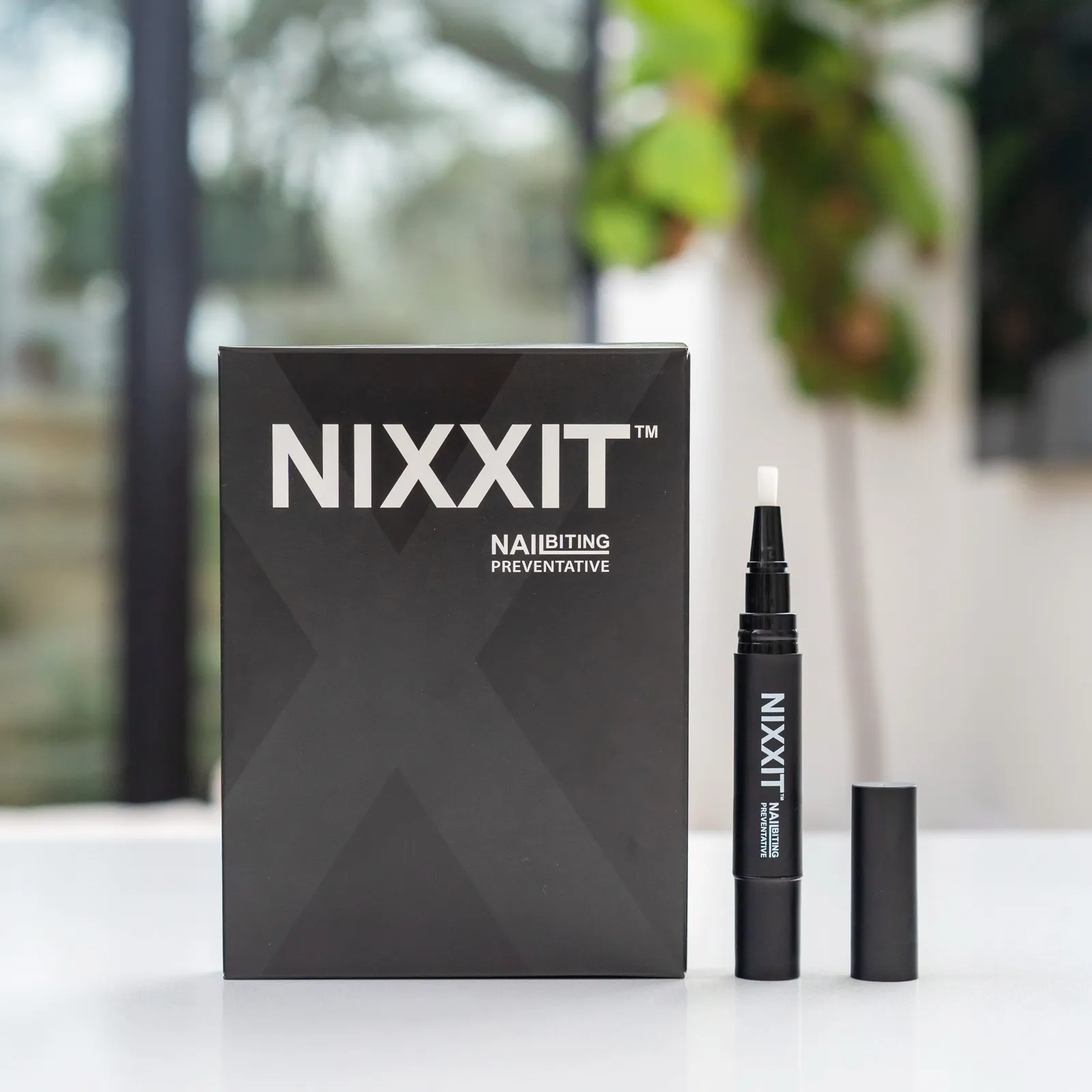The Nixxit carton and its twist-up applicator pen, photographed whole on a white table in daylight.