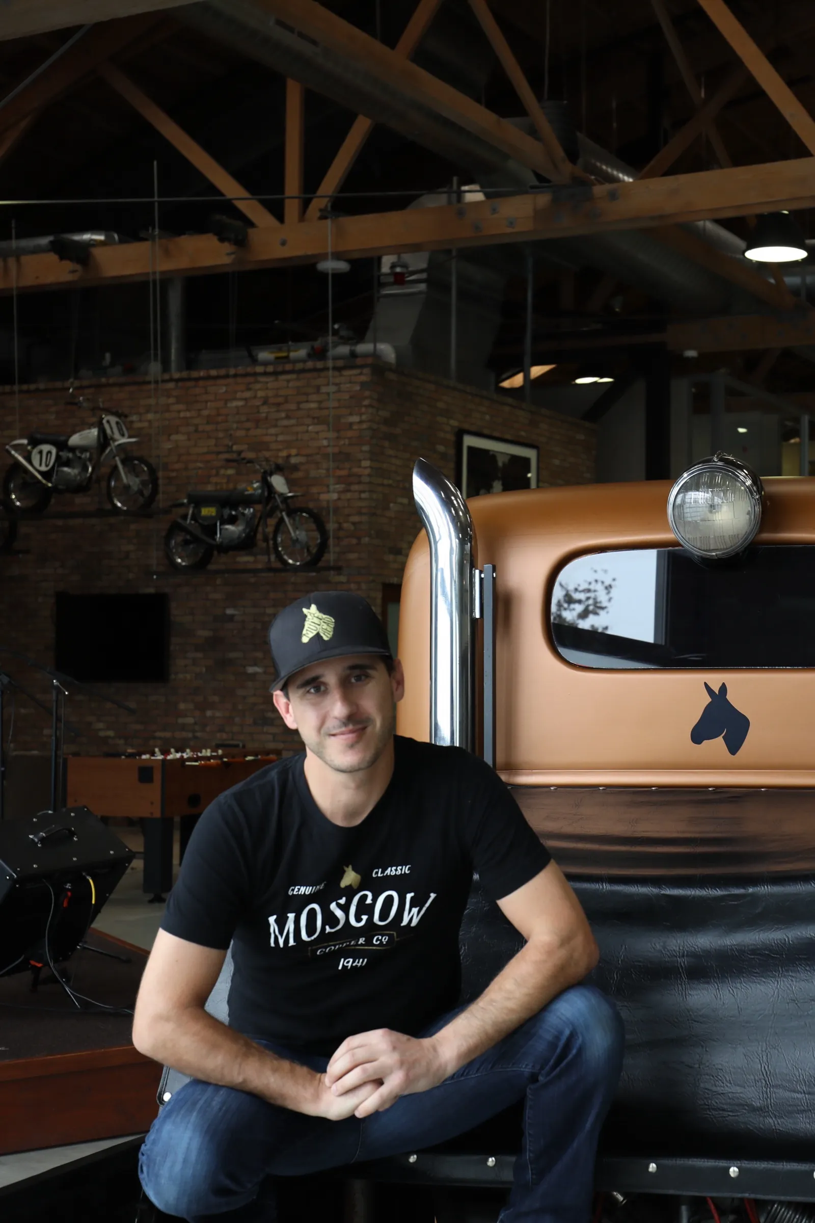 JJ Resnick seated on the bed of the restored Moscow Copper Co. cab-over truck in the company showroom, in a Moscow Copper Co. cap and shirt.